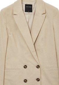 Beżowy sztruksowy blezer z dwurzędowym zapięciem, klapami z wycięciem oraz ciemnymi, okrągłymi guzikami. Zawiera boczne kieszenie i teksturowaną tkaninę.