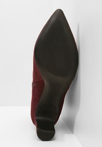 Chaussure en daim bordeaux avec un bout pointu et une silhouette élégante. Semelle en caoutchouc noire avec une texture antidérapante. Détail avec une fermeture éclair sur le côté.