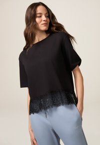Top negru scurt, cu mâneci scurte, detalii din dantelă la margine și text brodat. Asortat cu pantaloni de culoare albastră deschisă, cu un detaliu de text.