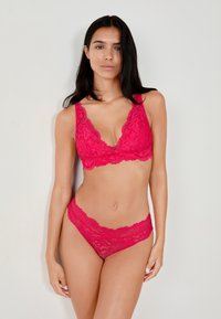 Set di lingerie in pizzo di un vivace colore rosa, composto da un bralette con scollatura a V profonda e mutandine abbinate con bordi ondulati e intricate fantasie floreali.