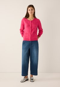 Felroze cardigan met een ronde hals, knoopsluiting aan de voorkant en geribbelde manchetten, gecombineerd met wijde denim broekspijpen en zilveren schoenen.