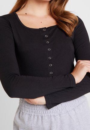 Schwarz langärmliges Oberteil mit rundem Ausschnitt und frontaler Druckknopfschließe; weicher Stoff mit glatter Textur und figurbetontem Design.