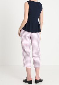 Námořnické peplum top s přiléhavým střihem, kombinované s kalhotami v růžovo-bílém houndstooth vzoru, které mají třásňové lemy, a černými lodičkami na podpatku.
