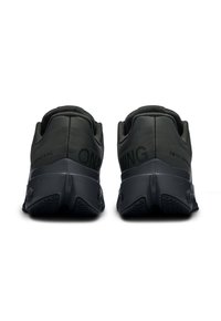 Chaussures de course noires avec une texture lisse, un col rembourré et un logo distinctif sur le talon. Présentent une semelle coussinée et une semelle extérieure texturée.