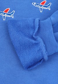 Niebieska bluza z haftowanym wzorem samolotu i czerwonymi akcentami. Tkanina jest gładka z textured ściągaczem.