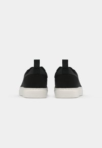 Tenisi negri cu partea superioară din material textil neted, talpă din cauciuc alb și o buclă la călcâi, având un design minimalist.