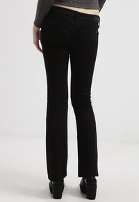 Czarne dżinsy z rozszerzanymi nogawkami charakteryzują się gładką fakturą, średnim stanem i dwoma tylnymi kieszeniami. Noszone z dopasowaną, szaro-długą bluzką z długim rękawem.