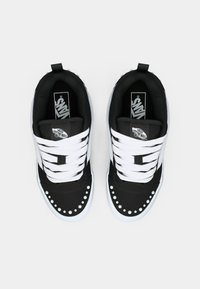 Černobílé tenisky s hladkým textilním svrškem, kulatými bílými cvočky podél špičky a bílými tkaničkami na ploché podrážce.