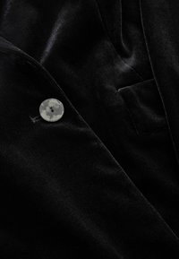 Schwarzer Samtstoff mit glatter Textur, versehen mit einem runden, marmorierten Knopf und einem subtilen Taschenakzent.