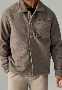 Grau melierte Fleecejacke mit einem Kragen, Knopfverschluss und einer einzelnen Brusttasche. Verfügt über ein strukturiertes Gewebe und Holzknöpfe.