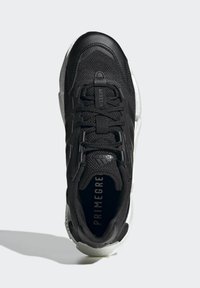 Zapatilla deportiva negra con una parte superior de malla texturizada, detalles de cuero sólido y una suela de goma blanca. Cuenta con cordones prominentes y un logotipo destacado.