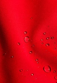 Wassertropfen perlen auf leuchtend rotem, strukturiertem, wasserdichtem Stoff und zeigen Oberflächenspannung sowie Stoffdetails.