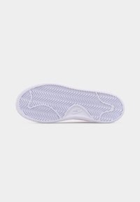 Semelle de chaussure Nike blanche avec motif de bande de roulement en zigzag et logo Nike en relief sur un fond gris clair uni.