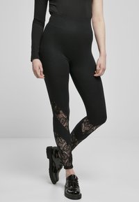 Leggings noirs avec une taille haute et des panneaux en dentelle transparente présentant un motif floral sur les côtés. Texture lisse.