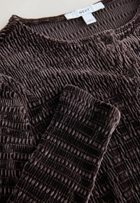 Pruun tekstuuriga kardigan lainelise mustriga, ümarate kaelustega ja kahe musta nupuga. Valmistatud pehmest, ribakanga materjalist.