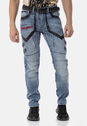 Ausgebleichte blaue Denim-Hosen mit schwarzen Kunstlederakzenten, mehreren Reißverschlusstaschen und roten Stickdetails. Gürtel mit Nieten inbegriffen.