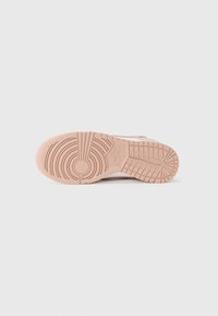 Suola di sneaker Nike in morbido gomma rosa, caratterizzata da modelli di trama circolari e lineari per trazione e aderenza. Superficie testurizzata con dettagli di branding.