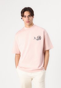 Light pink oversized T-shirt made of cotton, featuring a black and white graphic design on the chest. Short sleeves and crew neck.