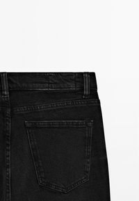 Vue arrière d’un jean en denim noir montrant la ceinture, les passants de ceinture et une seule poche arrière avec des coutures visibles.