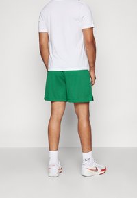 Gröna mesh atletiska shorts med sidofickor, kombinerat med en enkel vit t-shirt och vita atletiska skor med röda detaljer.