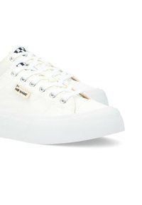 Sneaker bianchi in tela con suola in gomma testurizzata, dotati di occhielli in metallo argentato tondi, lacci bianchi e un'etichetta decorativa a scacchi bianco e nero.