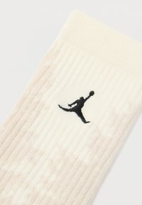 Meia creme canelada com um padrão bege subtil, apresentando um logo Jumpman bordado em preto perto do topo. Textura suave, com comprimento até à meia-coxa.
