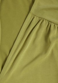 Gros plan d’un tissu vert olive avec un détail de couture froncée le long d’une couture créant des plis doux.