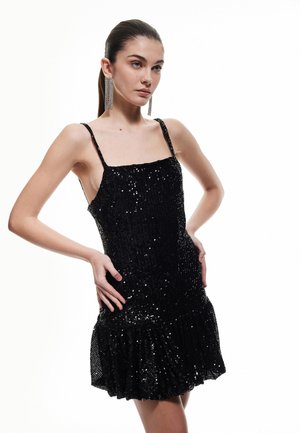 Robe noire à paillettes avec des fines bretelles, un corsage ajusté et un ourlet à volants, présentant une surface texturée et des détails réfléchissants.