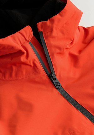 Chaqueta impermeable naranja con cuello alto, cremallera negra y textura suave; incluye acentos en negro contrastantes y detalles de costura.