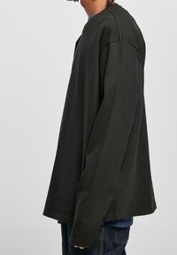 Black oversized long-sleeve shirt with a rounded neckline, soft texture, and drop shoulder seams, worn layered over a blue shirt.