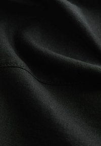 Gros plan sur un tissu noir montrant une texture fine et une couture avec des plis doux créant des contrastes de lumière et d'ombre.