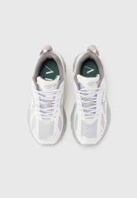 White athletic shoes featuring mesh panels, grey accents, and a textured sole. Laces are white; insoles are green with a logo outline.