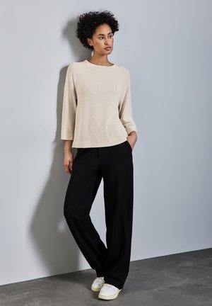 Beige struktureret pullover med bred halsudskæring, 3/4-ærmer, parret med sorte brede bukser og hvide sneakers. Enkel og minimalistisk design.