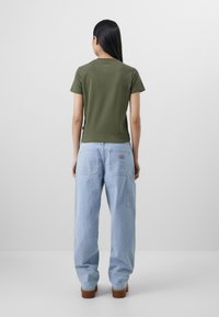 Green short-sleeve T-shirt paired with light blue, loose-fit denim jeans with large back pockets and a subtle brand logo above the right pocket.
