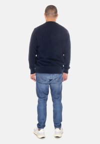 Maglione navy a collo rotondo, abbinato a jeans azzurri chiari. L'individuo indossa scarpe da ginnastica bianche, visto da dietro.