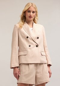 Blazer doppiopetto rosa chiaro con righe verticali, bottoni neri e due tasche frontali. Abbinato a pantaloni shorts a vita alta coordinati.