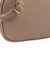 Lichtbeige leren tas met een gestructureerd oppervlak, afgeronde vorm en goudkleurige hardware aan het bandje. Opvallende stikdetails langs de randen.