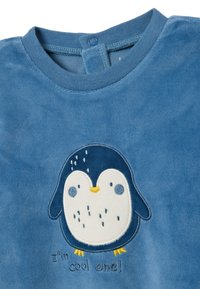 Sudadera de forro polar azul con un diseño de pingüino y detalles bordados. Texto "¡Soy el cool!" debajo del pingüino. Textura suave, cuello redondo.