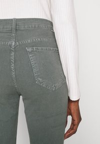 Grijze spijkerbroeken hebben een achterzak met een duidelijk omlijnd ontwerp. Het model draagt een geribbelde witte longsleeve.