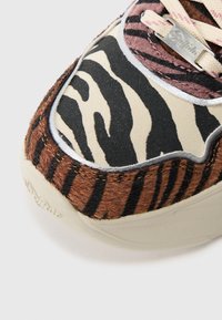Sneaker featuring a multi-patterned design with faux fur in tiger stripes, shades of brown, cream, and black, with metallic accents and beige sole.