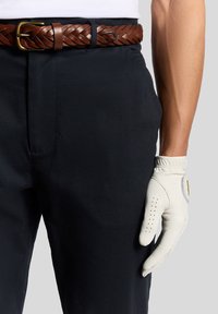 Pleteni smeđi kožni pojas u paru s tamnoplavim hlačama i svijetlosivom golf rukavicom s perforacijama za bolji grip te logotipom na zapešću.