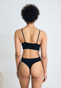 Zwarte naadloze bh met spaghettibandjes en bijpassende hoge taillestring, gemaakt van zachte, rekbare stof met een gladde textuur.