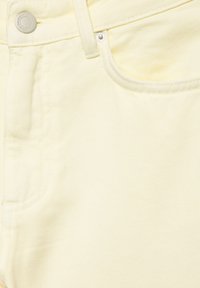 Gros plan sur un tissu en denim jaune montrant une poche avant, une boucle de ceinture et des boutons en métal sur un jean.