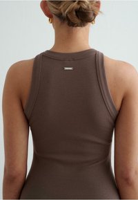 Brown ribbed tank top with a fitted design, featuring a subtle metallic logo detail on the back, showcasing a smooth texture.
