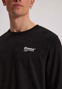 Czarny longsleeve wykonany z bawełny, z małym białym logo "Diverse ExtremeTeam.com" na lewej piersi. Okrągły dekolt.