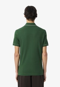 Polo verde con maniche corte, caratterizzato da un colletto bianco e bordini delle maniche bianchi. Realizzato in materiale morbido, presenta un design semplice e classico.