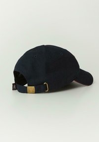 Granatowa czapka z zakrzywionym daszkiem, wykonana z bawełny. Posiada złotą metalową klamrę do regulacji oraz małą metkę z boku.