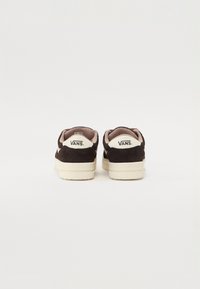 Black suede Vans sneakers with a cream rubber sole and pink lining, featuring a prominent white Vans logo on the heel.