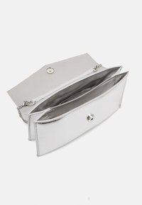 Pochette métallique argentée avec une texture lisse, dotée d'une fermeture à pression et d'un compartiment intérieur zippé, complétée par une bandoulière en chaîne.