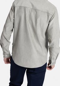 Camisa de botones en gris claro con finas rayas verticales. Mangas largas con puños abotonados y un dobladillo curvado en la parte trasera.